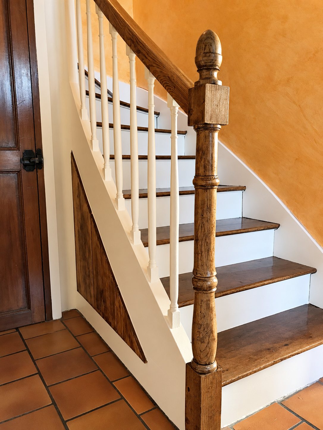 Un escalier intérieur rénové avec marches en bois, contremarches et balustres blancs, un gros poteau en chêne et un mur orangé.